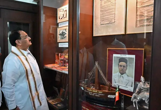 वी आर सावरकर की तस्वीर के साथ खड़े बीजेपी अध्यक्ष जेपी नड्डा