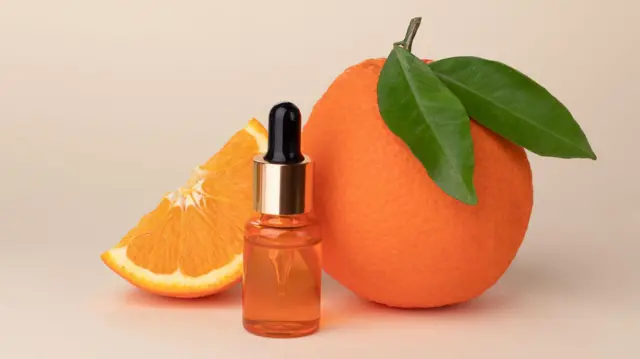 قنينة بها سائل برتقالي اللون تتوسط برتقالة وشريحة برتقال