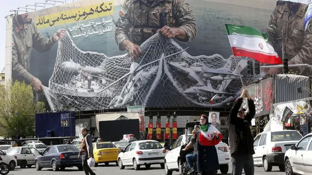 نمایی کلی از بنر عظیمی که در میدان انقلاب تهران آویخته شده و روی آن نوشته شده است: «تنگه هرمز همچنان بسته خواهد ماند؛ سراسر خلیج فارس میدان شکار ماست.» این تصویر در حالی ثبت شده که زندگی روزمره در تهران ۵ آوریل ۲۰۲۶ (۱۶ فروردین ۱۴۰۵) ادامه دارد.