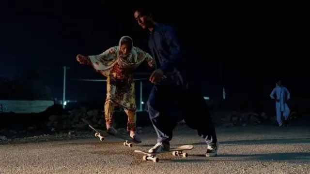 هوا تاریک است، چند نوجوان دختر و پسر در حال اسکیت سواری