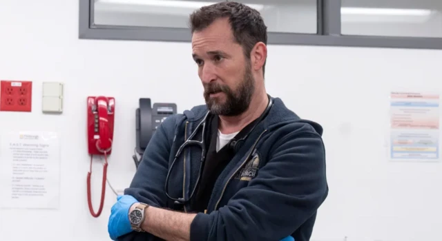 Un hombre con barba, un fonendoscopio colgado sobre el cuello y guantes de látex azul. 