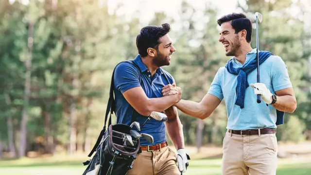 Dois homens se cumprimentam, alegres, em um campo de golfe
