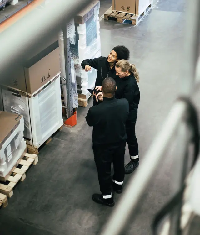 Дві жінки та чоловік стоять на складі між великими коробками і контейнерами