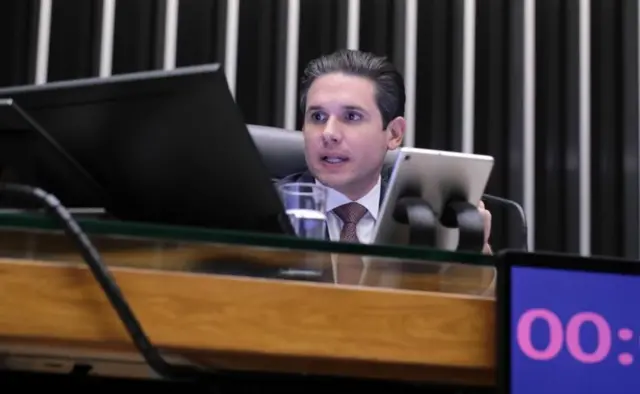 Hugo Motta observa algo, com olhar sério, na mesa diretora da Câmara