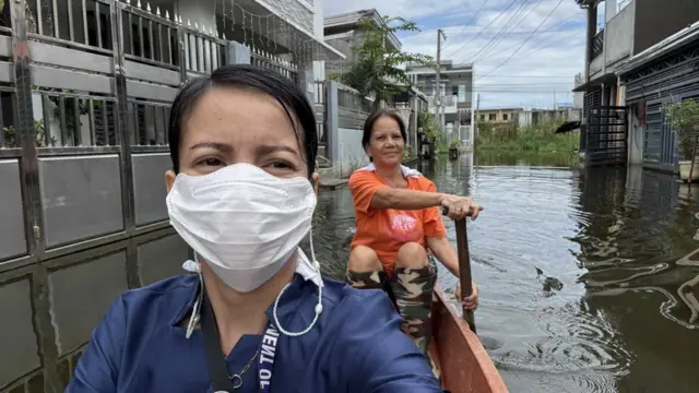 দুটি ভবনের মাঝখানে পানিতে ডুবে যাওয়া রাস্তা দিয়ে নৌকায় করে যাচ্ছেন দুই নারী