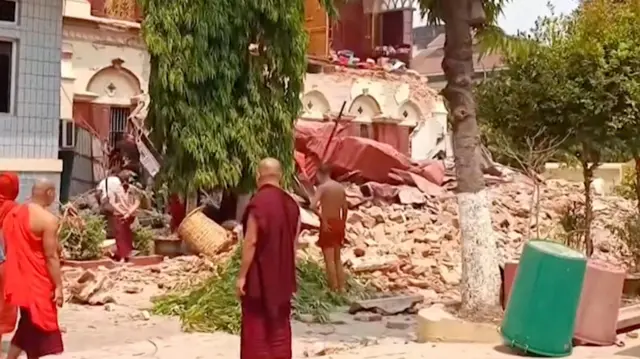 Pessoas vestindo mantos se reúnem perto de um templo desabado após o terremoto em Mandalay