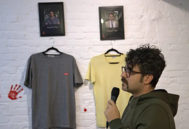 سوران منصورنیا در نمایشگاه «آنچه باقی ماند» در کلن، عکس و لباس برادرش روی دیوار آویزان شده است 