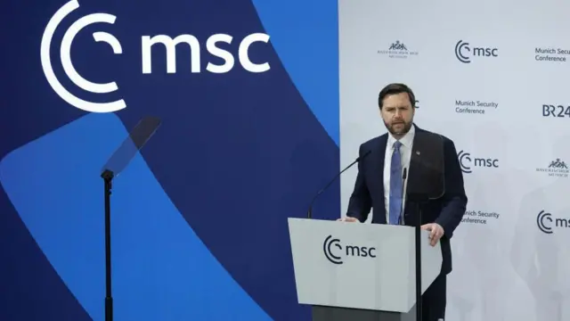 Вэнс на прошлогодней конференции в Мюнхене. Он стоит за трибуной и произносит речь Вэнс на прошлогодней конференции в Мюнхене. Он стоит за трибуной и произносит речь