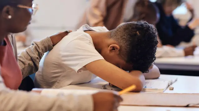 कक्षा में डेस्क पर सिर टिकाए उदास किशोर लड़के को सांत्वना देती छात्रा