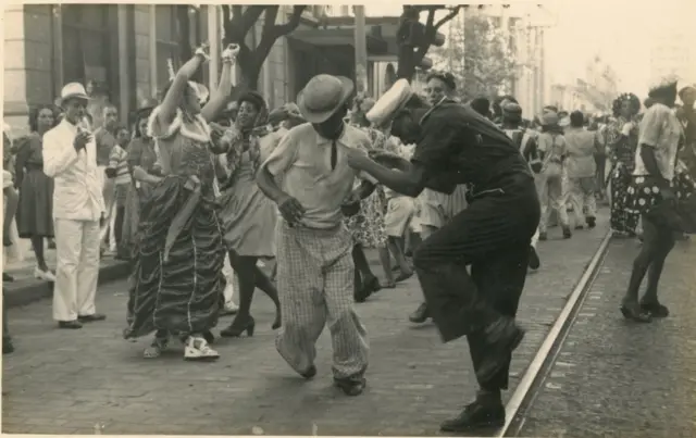 Fotografia em preto e branco mostra festa na avenida Rio Branco, no Rio de Janeiro, com pessoas fantasiadas e dançando na rua