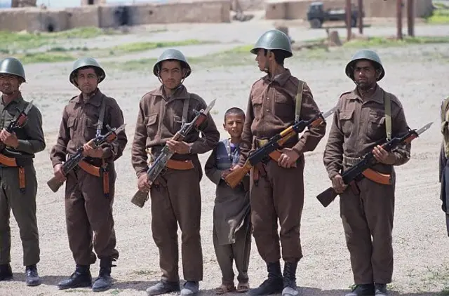 سربازان ارتش در حومه شهر هرات، ۲۴ اپریل ۱۹۹۲، اسلحه کلاشینکوف در دست دارند و یک کودک هم در مان آنان ایستاده است 