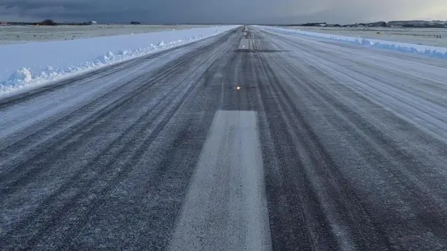 Muestra una pista de aeropuerto con nieve a ambos lados.