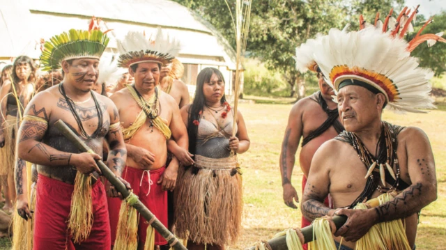 Indígenas do povo zoró adornados com cocares e objetos ritualísticos durante apresentação