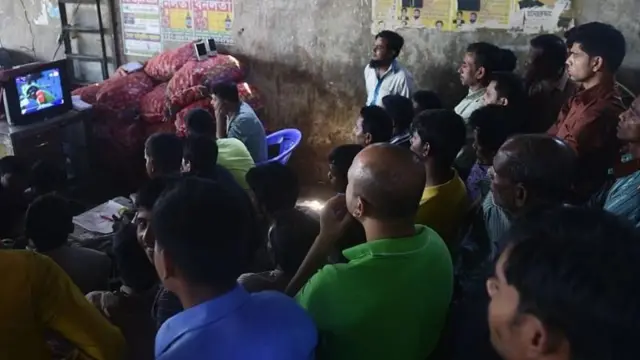 কয়েকজন লোক চেয়ারে বসে টেলিভিশন দেখছেন