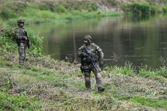 Двоє чоловіків у військовій формі зі зброєю та бронежилетами з написом "Страж Гранічна" (тобто Прикордонна служба) патрулюють берег озера
