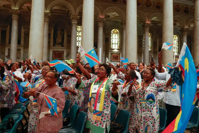 Une congrégation composée principalement de femmes de la RD Congo qui acclament dans la Basilique papale de Saint-Paul-hors-les-Murs à Rome, certaines agitant des drapeaux congolais, lors de la cérémonie de béatification de Floribert Bwana Chui Bin Kositi en juin.