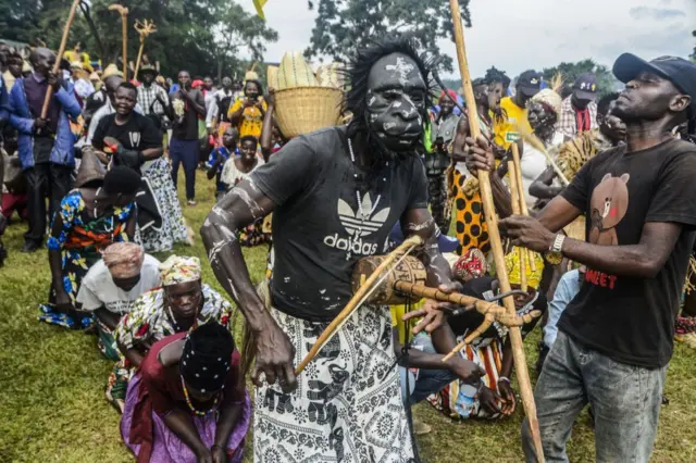 Umugabo urimo gucuranga igikoresho gakondo ari kumwe n'abandi bantu