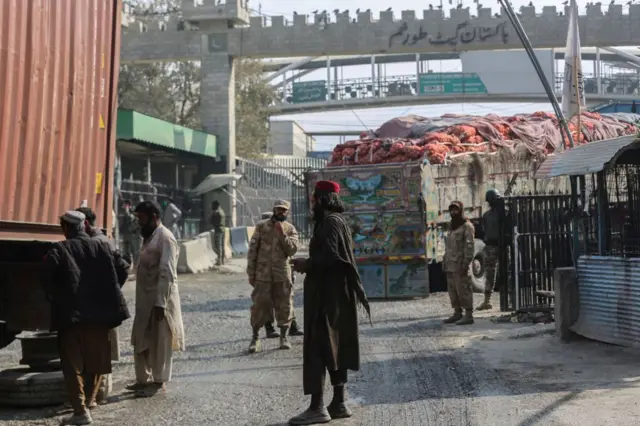 عکس دروازه تورخم میان افغانستان و پاکستان را نشان می‌دهد. در حالی که نیروهای امنیتی دو طرف در تصویر دیده می‌شوند و یک لاری بزرگ حامل اموال تاجران در حال عبور از دروازه است.