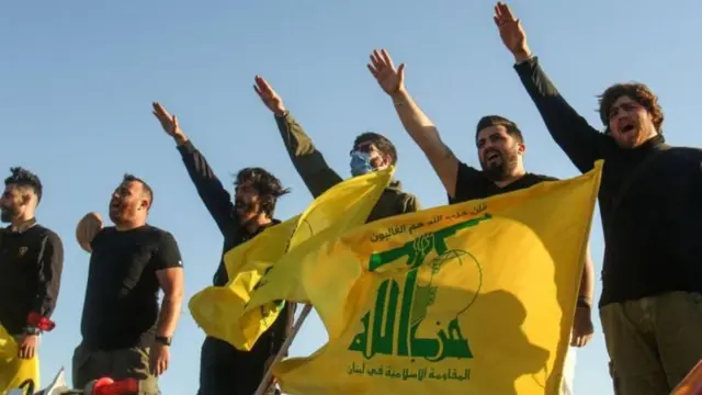 Homens erguendo braço e segurando bandeira do Hezbollah