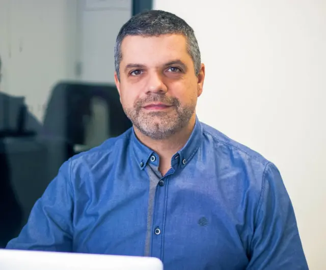 Denicoli usa uma camisa azul e olha para a foto