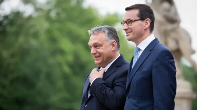 Dwaj mężczyźni w niebieskich garniturach uśmiechają się, spacerując po parku.