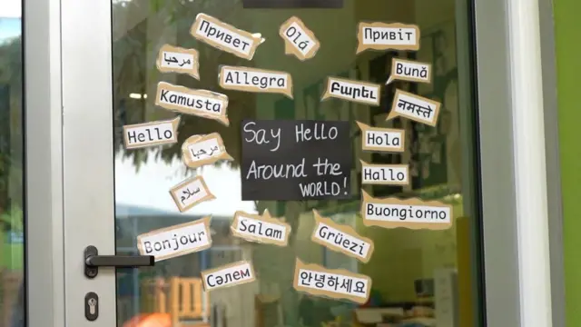 صورة تُظهر باباً زجاجياً لإحدى المدارس عليه شعارات بمختلف اللغات ومن بينها العربية مكتوب عليها