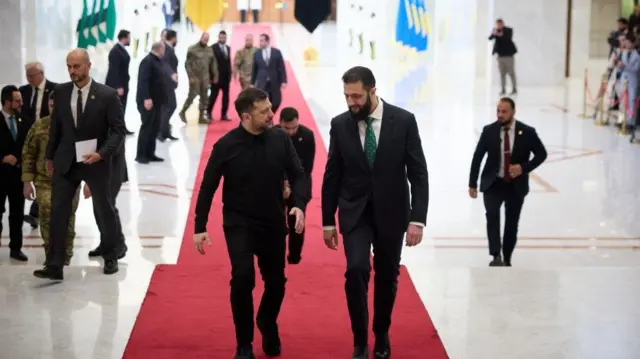 Зеленський та Аш-Шараа прямують червоною доріжкою. Ліворуч - український президент, праворуч - сирійський. Обидва в чорних костюмах. 