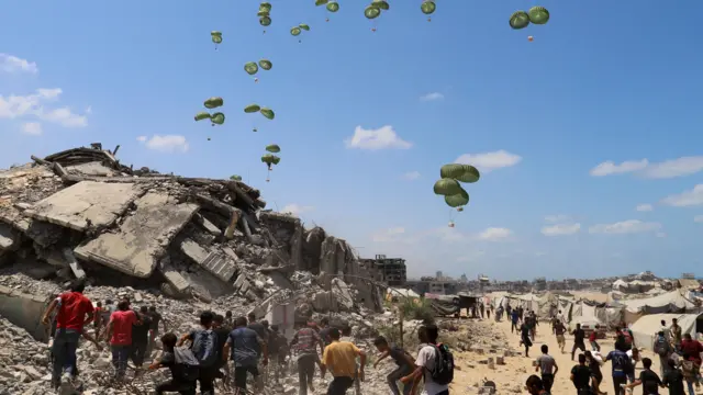 Palestinos correm em direção a paraquedas carregando pacotes de ajuda humanitária lançados de avião sobre o norte da Faixa de Gaza, em 7 de agosto de 2025
