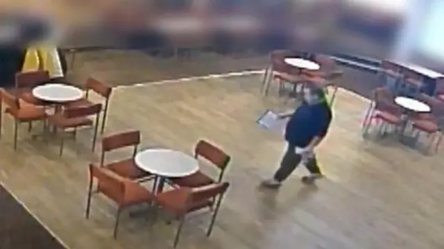 A man in a blue top on CCTV walking across a social club