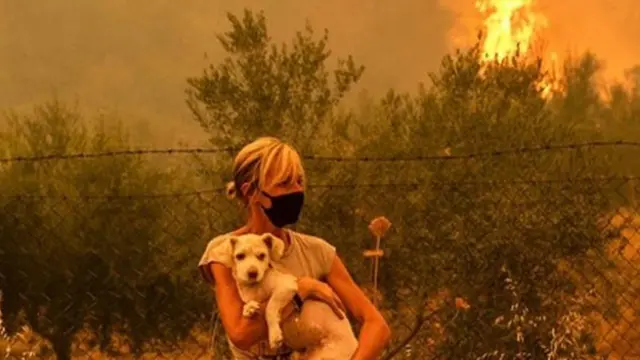 Wata mata dauke da kare yayin da wutar daji ke ci a bayanta a Girka