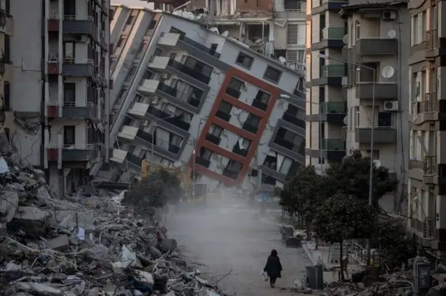 A woman walks alone among destroyed buildings in Hatay. Girgizar ƙasa ta kashe dubban Turkawa tare da raunata wasu da yawa bayan ta afka wa kudu maso gabashin ƙasar da ke iyaka da Syria a watan Fabrairu.