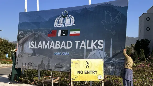 A large, blue road-side sign which reads: Islamabad Talks, April 2026. 