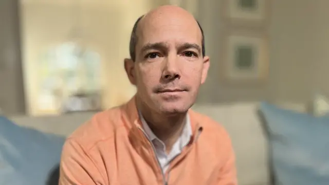 Rodney Miller wearing a white shirt and orange pullover