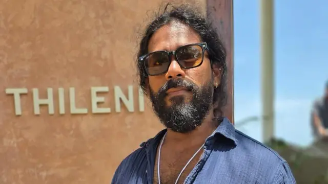 Thileni's නමැති ආපනශාලාවේ හිමිකරු නිල් පැහැති කමිසයක් ඇඳ අව් කන්නාඩි පැළඳ සිටියි