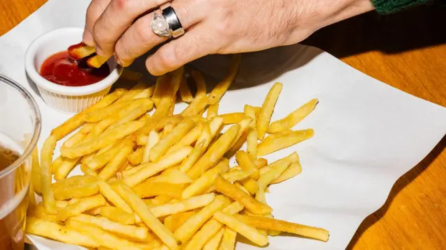 mão com anel no dedo molhando batatas fritas em molho de ketchup