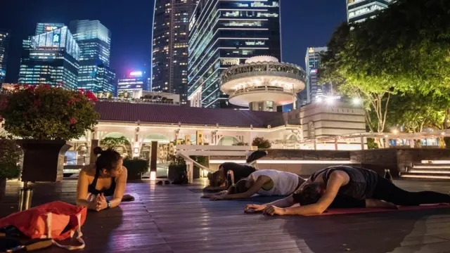 Pessoas fazendo exercício à noite, ao ar livre e em um tapete, em ambiente urbano