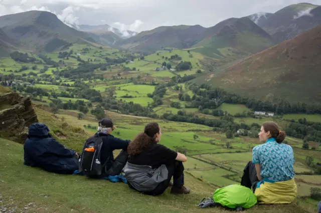Wędrowcy jedzą lunch i podziwiają widok ze Skellgill Bank of Swinside i Derwent Fells poniżej w Lake District National Park,