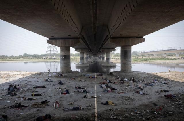 أشخاص ينامون على مجرى نهر يامونا تحت جسر في يوم صيفي حار في دلهي، الهند.