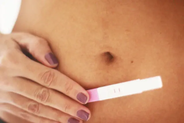 mulher com teste de gravidez positivo encostado em sua barriga