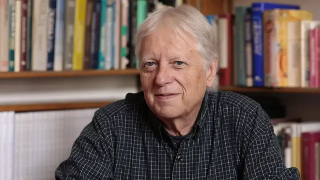 Mark Rank com camisa escura, em frente a uma estante de livros