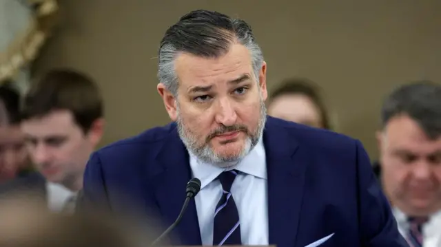 Sịnetọ a ma-ama na mba Amerịka bụ Ted Cruz ji akụrụngwa e ji ekwu okwu a na-akpọ 'microphone' n'okwu bekee n'ihu ya dịka ndị mmadụ tukwuru ala n'akụkụ ya. O yi uwe elu na-acha anụnụ anụnụ na uwe elu ọcha nwere taị 