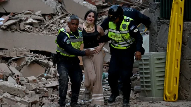 İki polis memuru yıkılan bir binanın enkazından sağ kurtulan bir kadını taşıyor