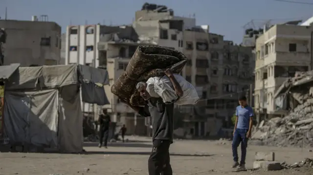 어깨에 짐을 지고 무너진 건물 잔해가 널린 가자 시티 거리를 걷는 남성의 모습