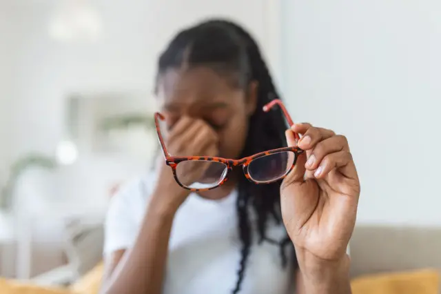 Une femme avec des lunettes porte la main à son nez