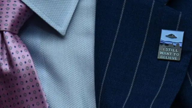 Uçan daire görüntüsü ve 'inanmak istiyorum'yazılı bir rozet