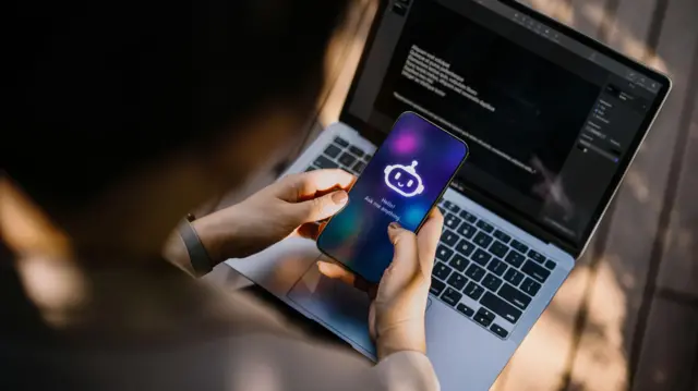 شخص يحمل هاتفاً تظهر على شاشته روبوت دردشة يعمل بالذكاء الاصطناعي يقول: 