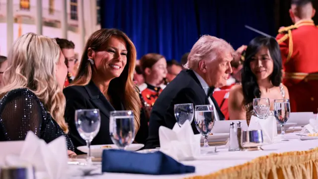 Zdjęcie Donalda Trumpa i Melanii Trump siedzących przy długim stole z białym obrusem, z innymi gośćmi siedzącymi wokół nich.
