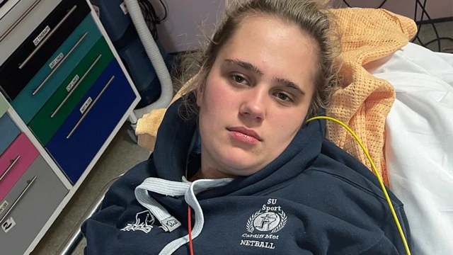 Phoebe Tesoriere deitada em uma cama de hospital, com agasalho azul