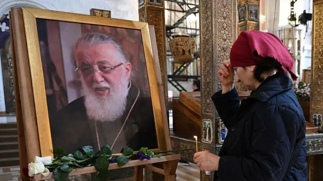 Женщина крестится у портрета Илии II