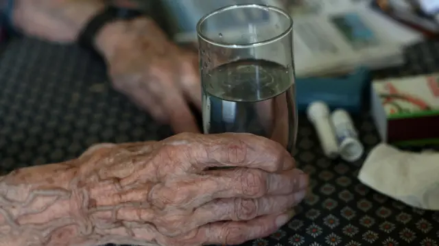 مريضة مسنة تحمل كوب ماء في باييه، جنوب غرب فرنسا، في 15 أغسطس/آب 2025. خلال موجة الحر، تدعو الممرضات الخاصات، اللواتي يقمن بجولات يومية لضمان استمرارية الرعاية في منازل المرضى، الذين غالباً ما يكونون من كبار السن والمعزولين، إلى توخي الحذر فيما يتعلق بهؤلاء الأشخاص الضعفاء، المعرضين بشكل خاص لمخاطر ارتفاع درجات الحرارة.